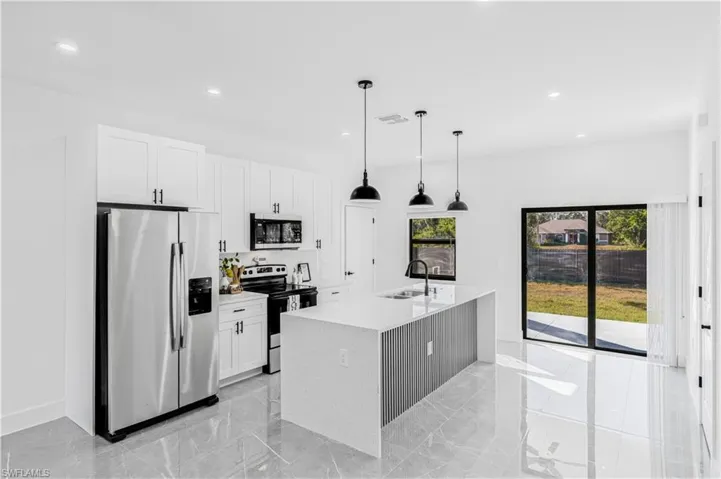 Kitchen with stainless steel appliances, white cabinets, light stone counters, an island with sink, and decorative light fixtures