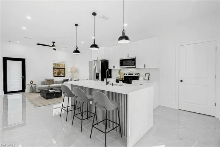 Kitchen featuring a kitchen island with sink, a breakfast bar area, white cabinetry, stainless steel appliances, and open floor plan