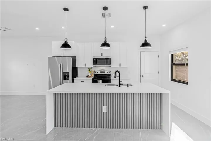 Kitchen featuring light stone counters, stainless steel appliances, white cabinets, a center island with sink, and a breakfast bar