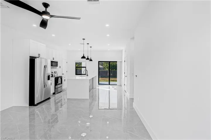 Kitchen featuring stainless steel appliances, a center island with sink, a ceiling fan, pendant lighting, and white cabinetry