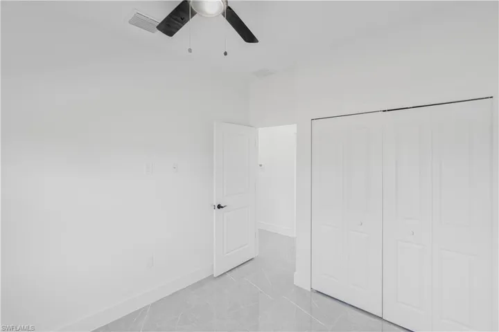 Unfurnished bedroom featuring ceiling fan, a closet, and light marble finish flooring