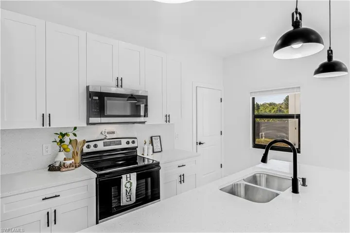 Kitchen featuring stainless steel appliances, white cabinetry, hanging light fixtures, and light stone countertops