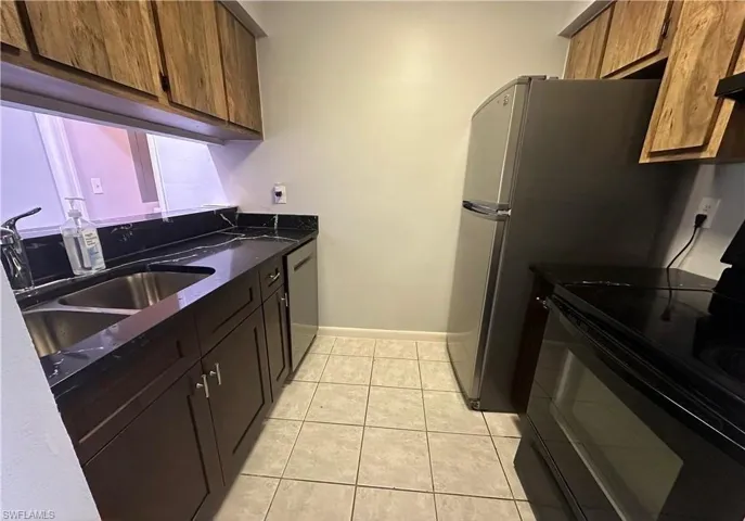 Kitchen with black / electric stove, dark stone counters, light tile patterned floors, and dishwasher