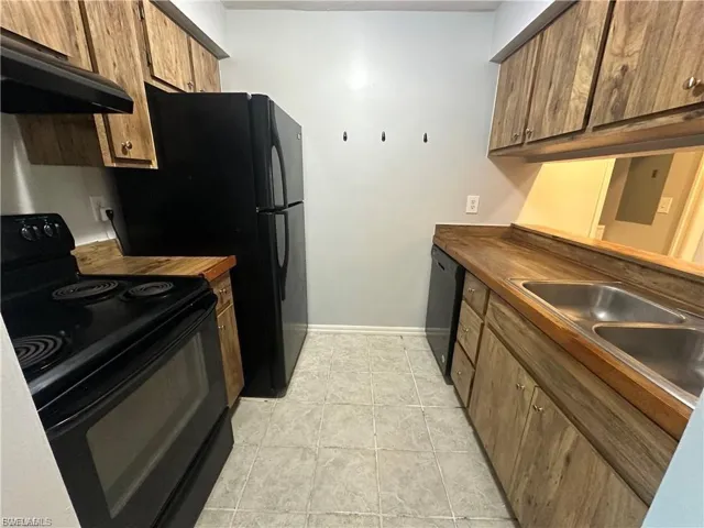 Kitchen featuring black appliances, under cabinet range hood, light tile patterned floors, wooden counters, and brown cabinetry