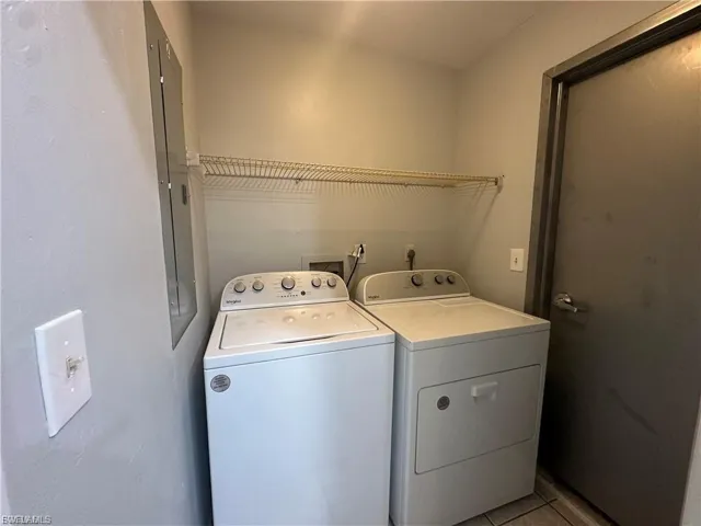 Laundry room with light tile patterned floors, electric panel, and washer and clothes dryer