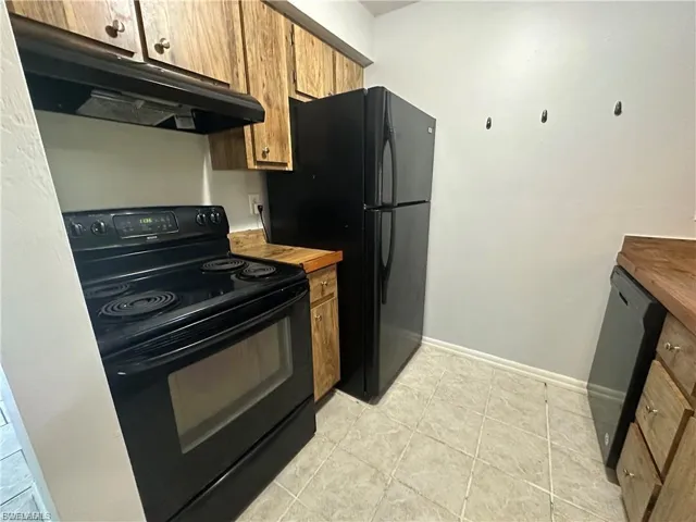 Kitchen with black appliances, butcher block countertops, under cabinet range hood, brown cabinetry, and light tile patterned flooring