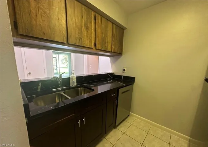 Kitchen with light tile patterned floors, stainless steel dishwasher, and dark stone countertops