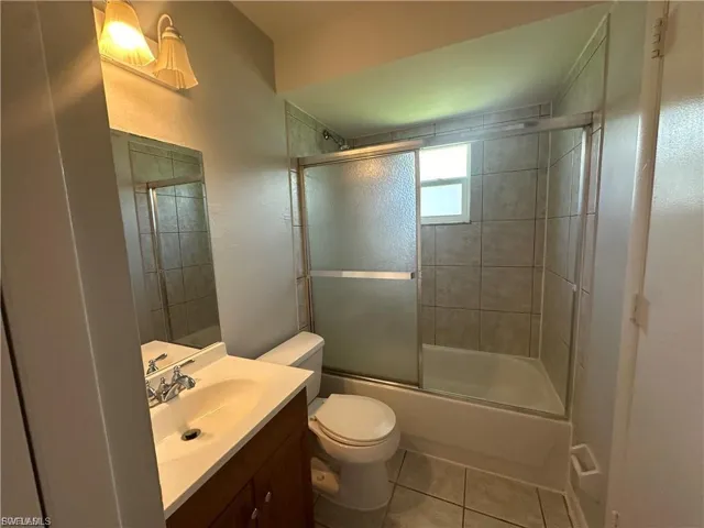 Bathroom featuring bath / shower combo with glass door, vanity, and light tile patterned floors