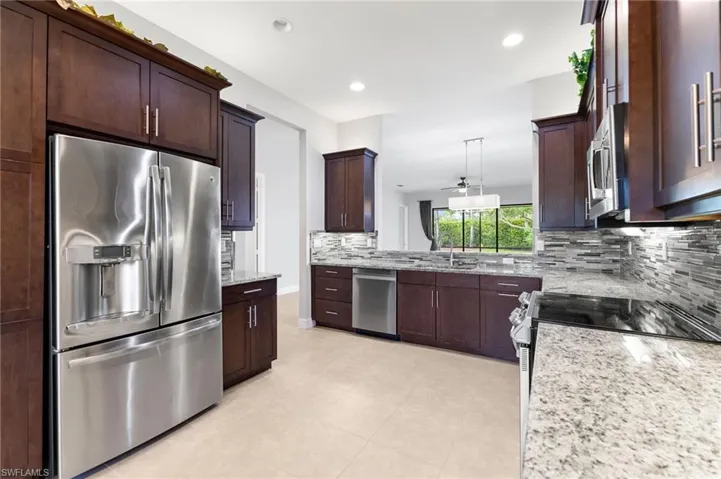 Kitchen with sink, appliances with stainless steel finishes, light stone counters, and backsplash