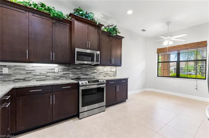 Kitchen featuring tasteful backsplash, stainless steel appliances, dark brown cabinets, light tile patterned floors, and ceiling fan