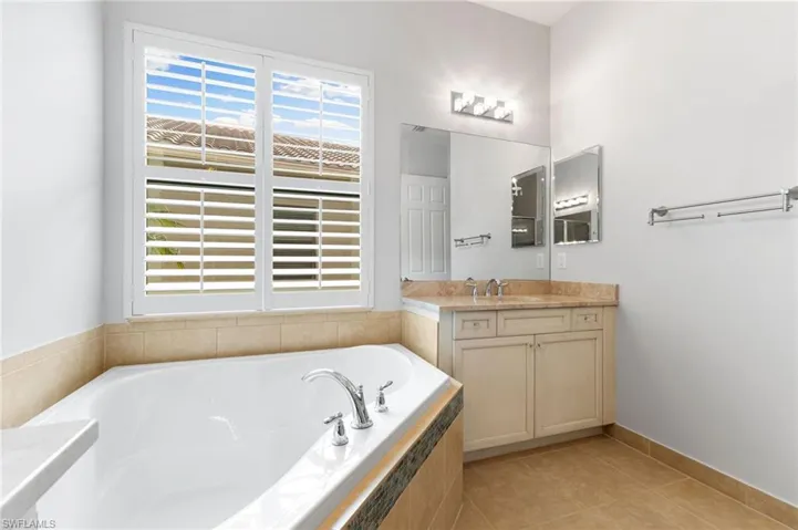 Bathroom featuring tiled tub, vanity, tile patterned floors, and a wealth of natural light