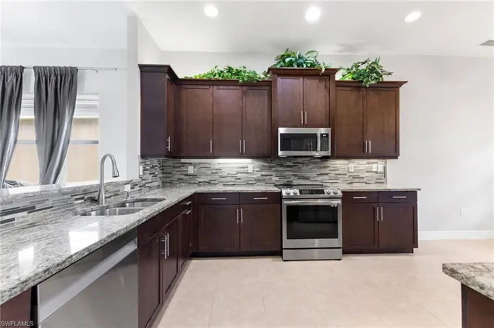 Kitchen featuring sink, tasteful backsplash, light stone counters, and stainless steel appliances