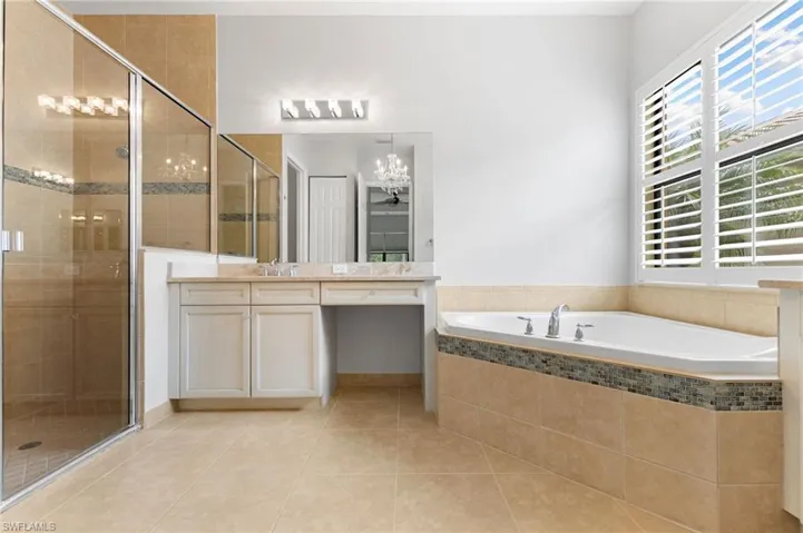 Bathroom with tile patterned flooring, separate shower and tub, a notable chandelier, and vanity