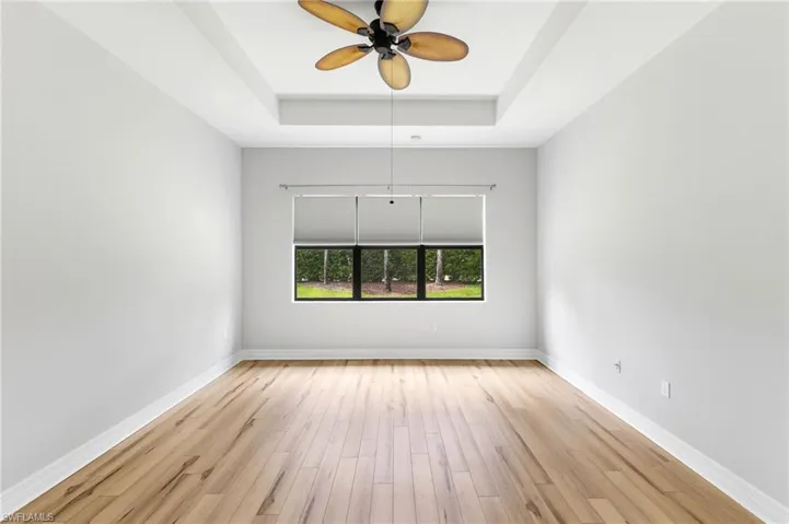 Unfurnished room featuring light hardwood / wood-style flooring, ceiling fan, and a raised ceiling