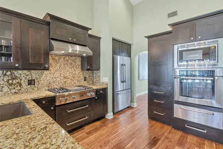 Kitchen featuring dark brown cabinets, light hardwood / wood-style flooring, stainless steel appliances, a high ceiling, and light stone countertops