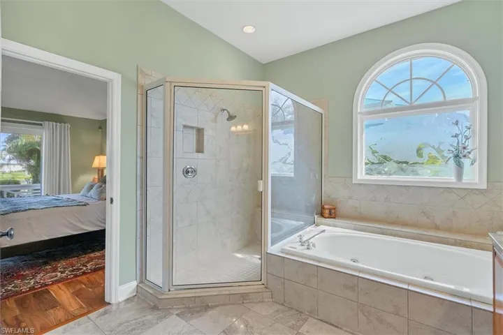 Bathroom featuring vaulted ceiling, plus walk in shower, and plenty of natural light