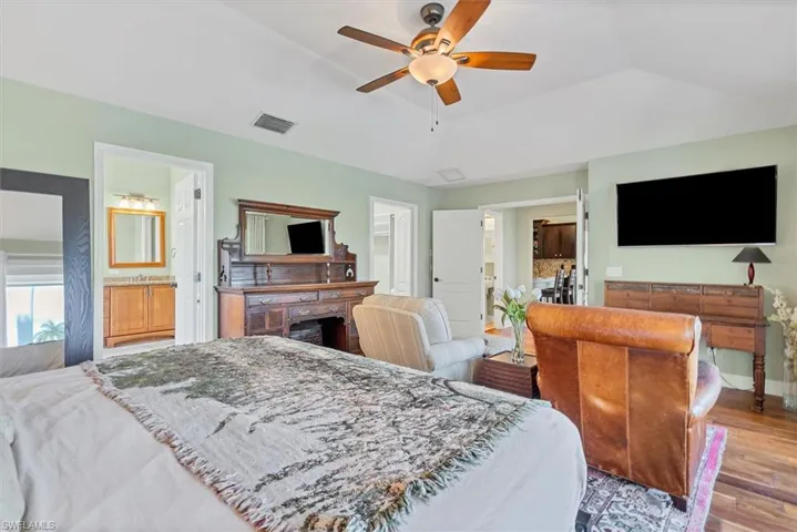 Bedroom with ceiling fan, a raised ceiling, ensuite bath, and light hardwood / wood-style floors
