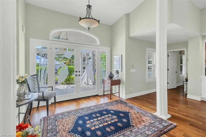 Foyer entrance featuring high vaulted ceiling, decorative columns, hardwood / wood-style flooring, and french doors