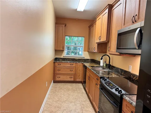 Kitchen featuring sink, dark stone countertops, light tile floors