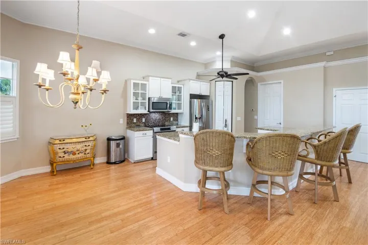 Kitchen featuring light hardwood / wood-style flooring, appliances with stainless steel finishes, ceiling fan with notable chandelier, white cabinets, and decorative light fixtures