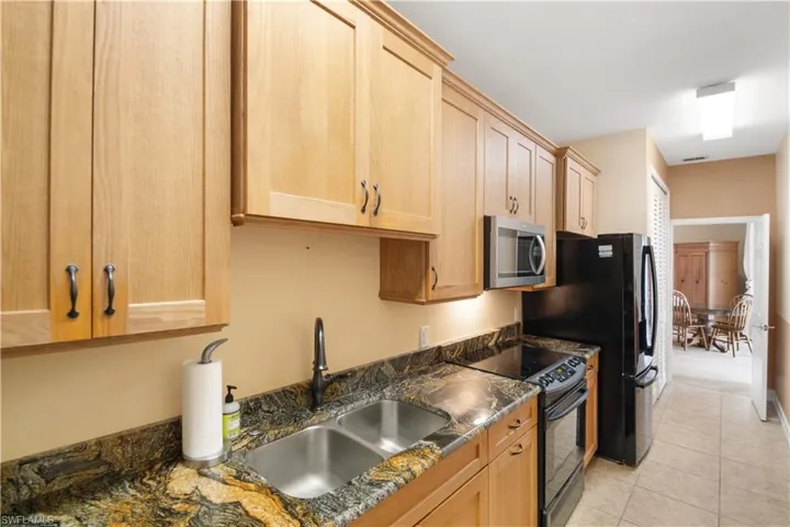 Kitchen featuring dark stone counters, light brown cabinetry, light tile floors, and sink