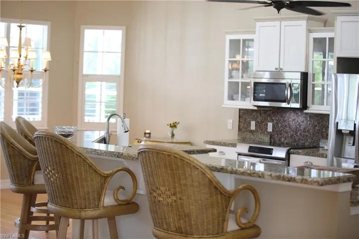 Kitchen with light hardwood / wood-style flooring, ceiling fan with notable chandelier, tasteful backsplash, a breakfast bar area, and appliances with stainless steel finishes