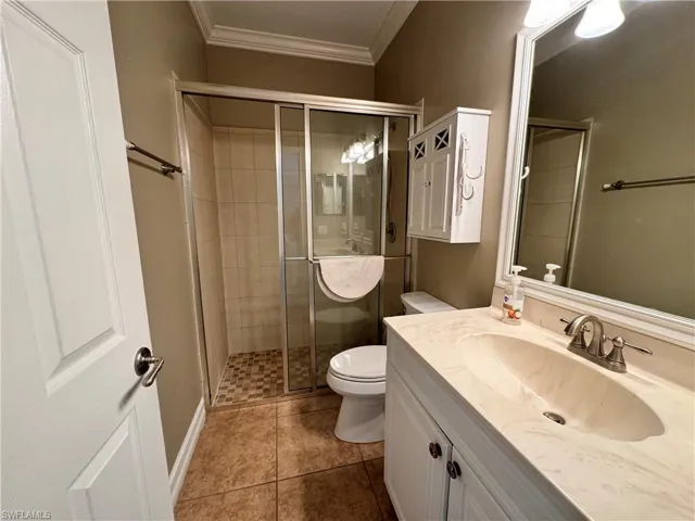 downstairs Bathroom with large vanity, tile flooring, toilet, and a shower with door