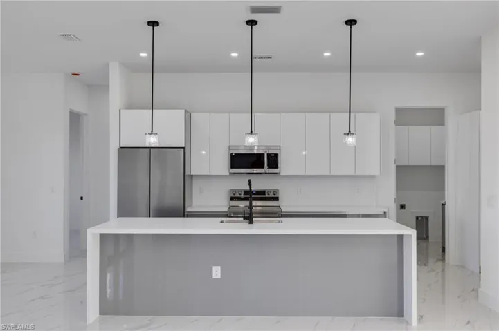 Kitchen featuring light marble finish flooring, light stone counters, stainless steel appliances, a center island with sink, and recessed lighting