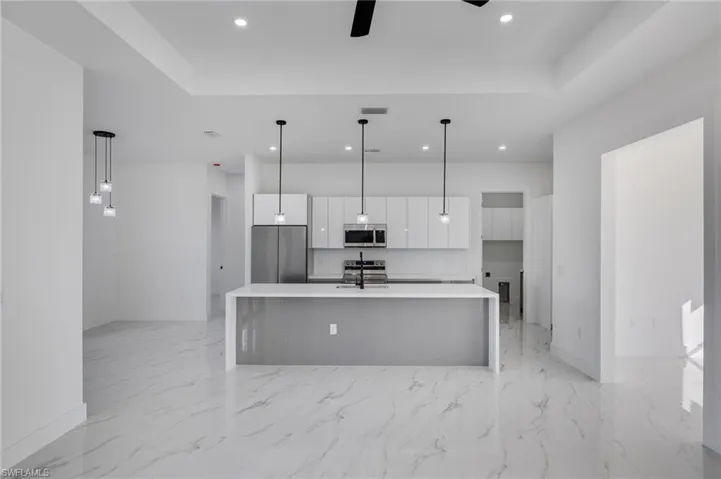 Kitchen with white cabinetry, a center island with sink, pendant lighting, stainless steel appliances, and modern cabinets