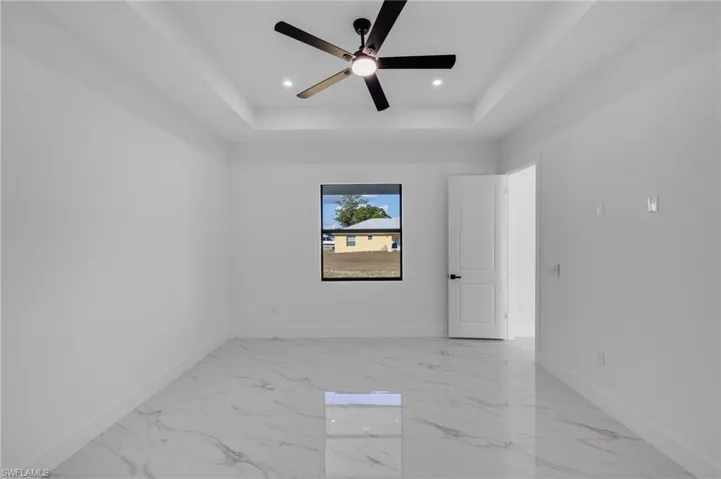 Unfurnished room with a raised ceiling, light marble finish flooring, ceiling fan, and recessed lighting