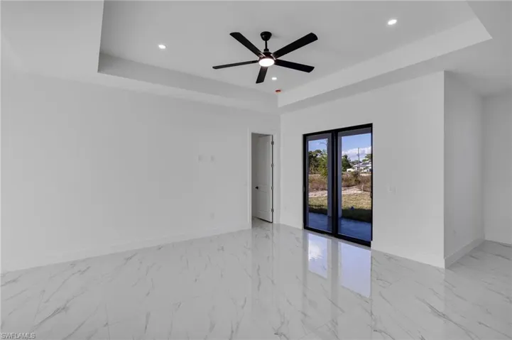 Empty room with light marble finish floors, a raised ceiling, recessed lighting, and a ceiling fan