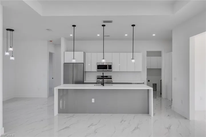 Kitchen with decorative light fixtures, appliances with stainless steel finishes, white cabinets, modern cabinets, and a center island with sink