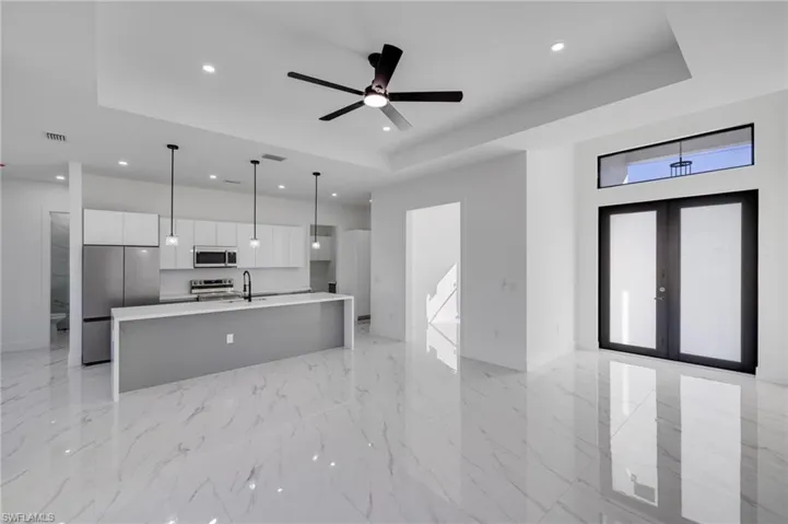 Kitchen with a large island with sink, white cabinetry, stainless steel appliances, open floor plan, and a raised ceiling