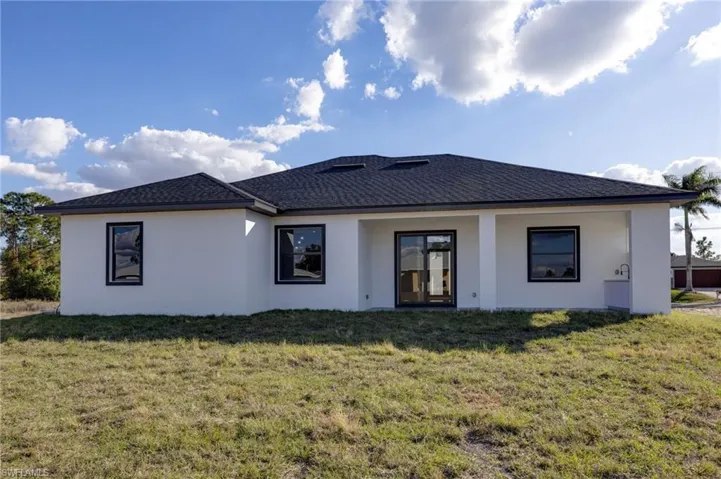 Rear view of property with a yard, stucco siding, and roof with shingles