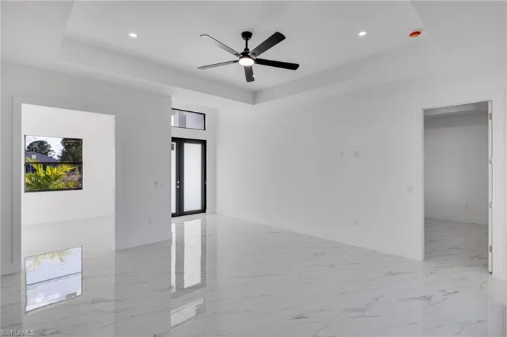 Spare room featuring a tray ceiling, light marble finish flooring, recessed lighting, ceiling fan, and french doors