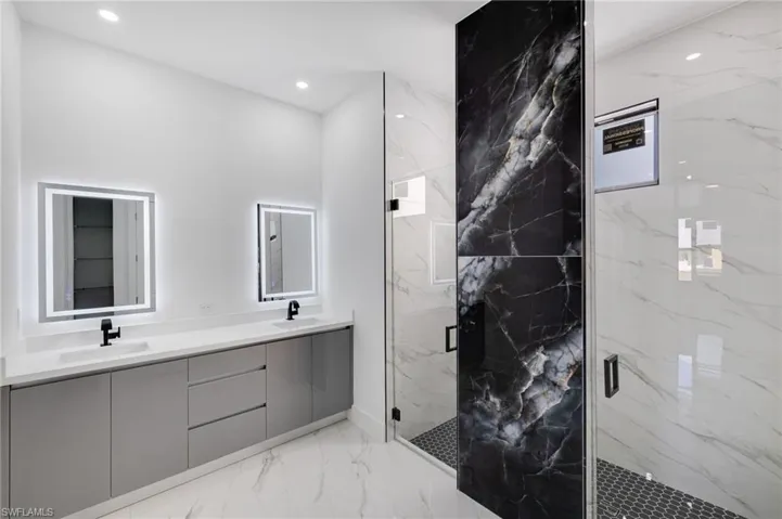 Full bath with double vanity, light marble finish floors, a marble finish shower, and recessed lighting