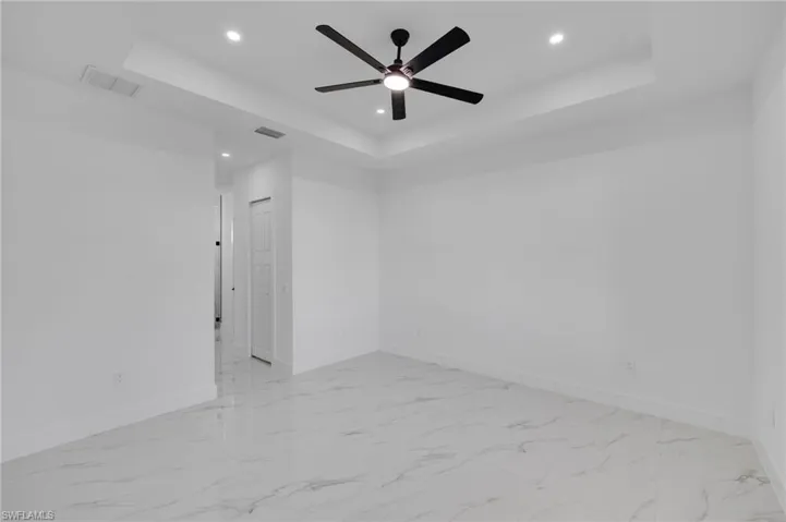 Empty room with a raised ceiling, recessed lighting, a ceiling fan, and light marble finish floors