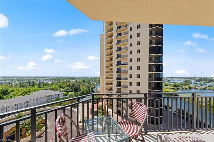 The property features a balcony with metal railings, offering views of the distant water and surrounding trees under a blue sky with clouds