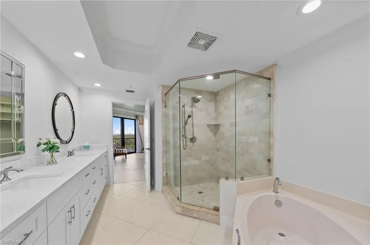 This bathroom features a double vanity with ample storage, a glass-enclosed shower with tile surround, and a built-in bathtub