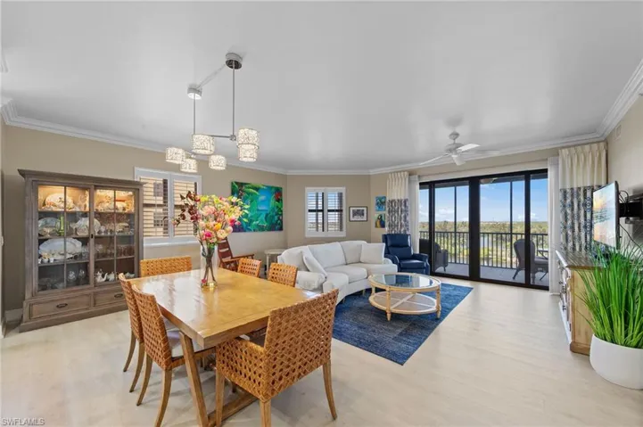 This open-concept living area features light-toned flooring, a dining space with a rectangular wooden table, and a living area with a large sofa