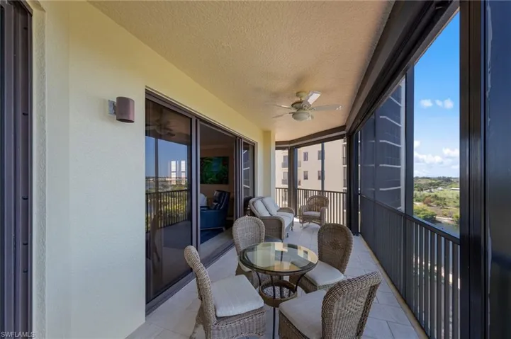 Expansive screened-in balcony featuring a ceiling fan, a tiled floor, and views of surrounding buildings and landscape