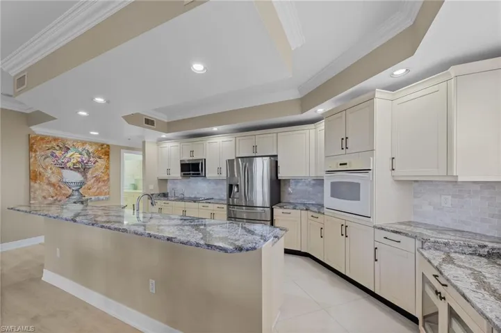 The kitchen features an expansive island with granite countertops, light-colored cabinetry, stainless steel appliances, and recessed lighting