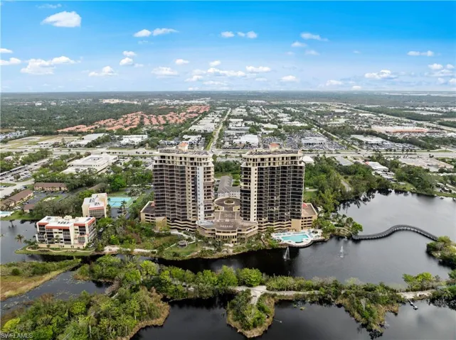 Aerial view of the property and its surrounding area, featuring two high-rise buildings, a large body of water, and lush green landscaping