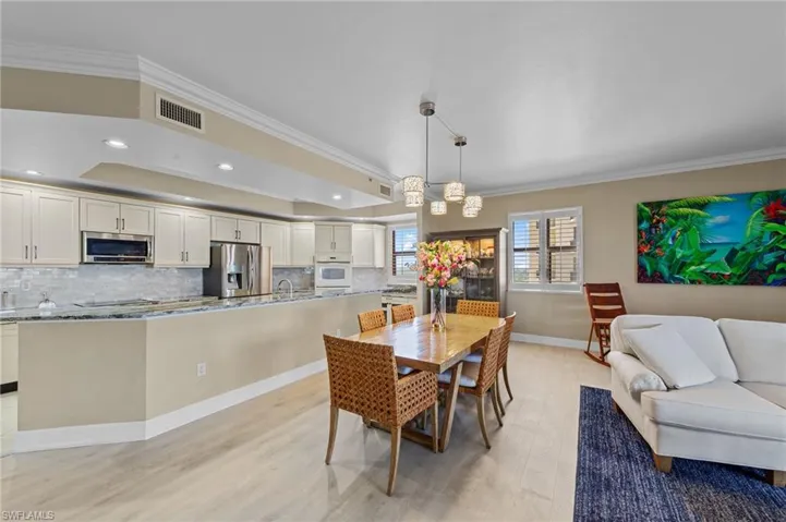 Open concept living space featuring light-toned flooring, recessed lighting, and a modern kitchen with a breakfast bar, light cabinetry, stainless steel appliances, and a tiled backsplash