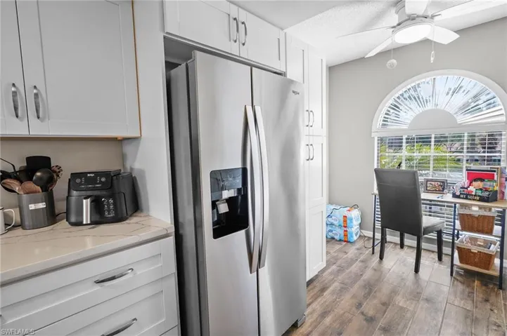 Kitchen with stainless steel fridge with ice dispenser, white cabinetry, dark wood-type flooring, ceiling fan, and light stone countertops