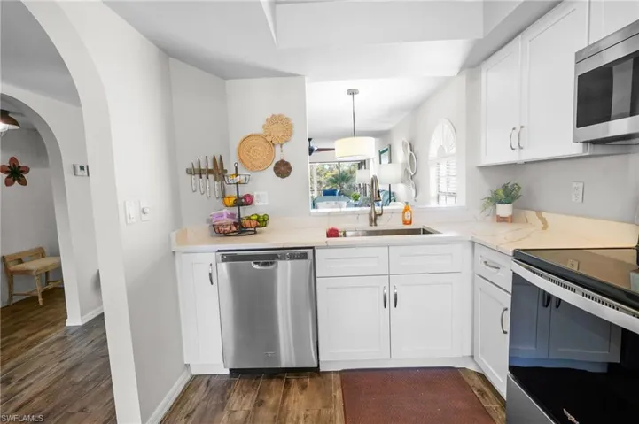 Kitchen with white cabinetry, stainless steel appliances, arched walkways, and dark wood-type flooring