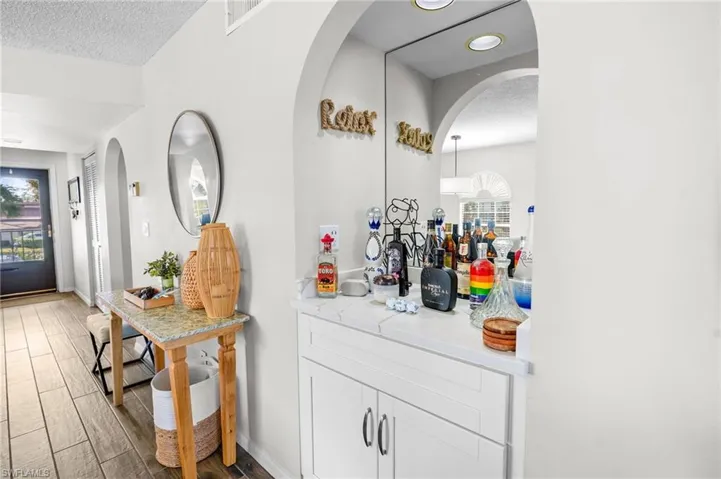 Bar area featuring white cabinets, arched walkways, wood finish floors, and a textured ceiling