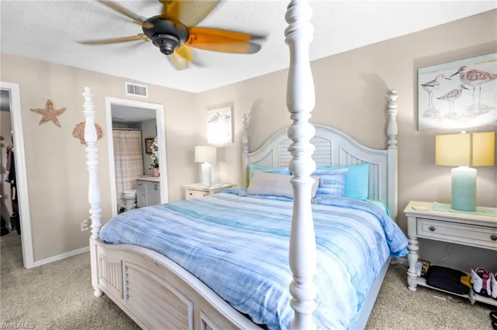 Bedroom with a walk in closet, light colored carpet, a ceiling fan, a textured ceiling, and connected bathroom