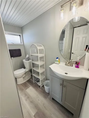 Vanity with integrated sink, wood-finish flooring, round mirror, and ceiling paneling