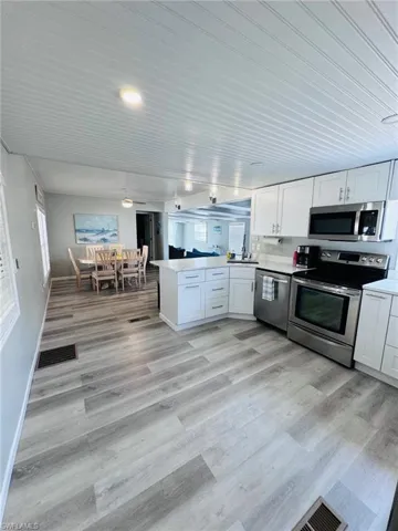 Open-concept layout featuring wood-finish flooring, white cabinetry, and stainless steel appliances